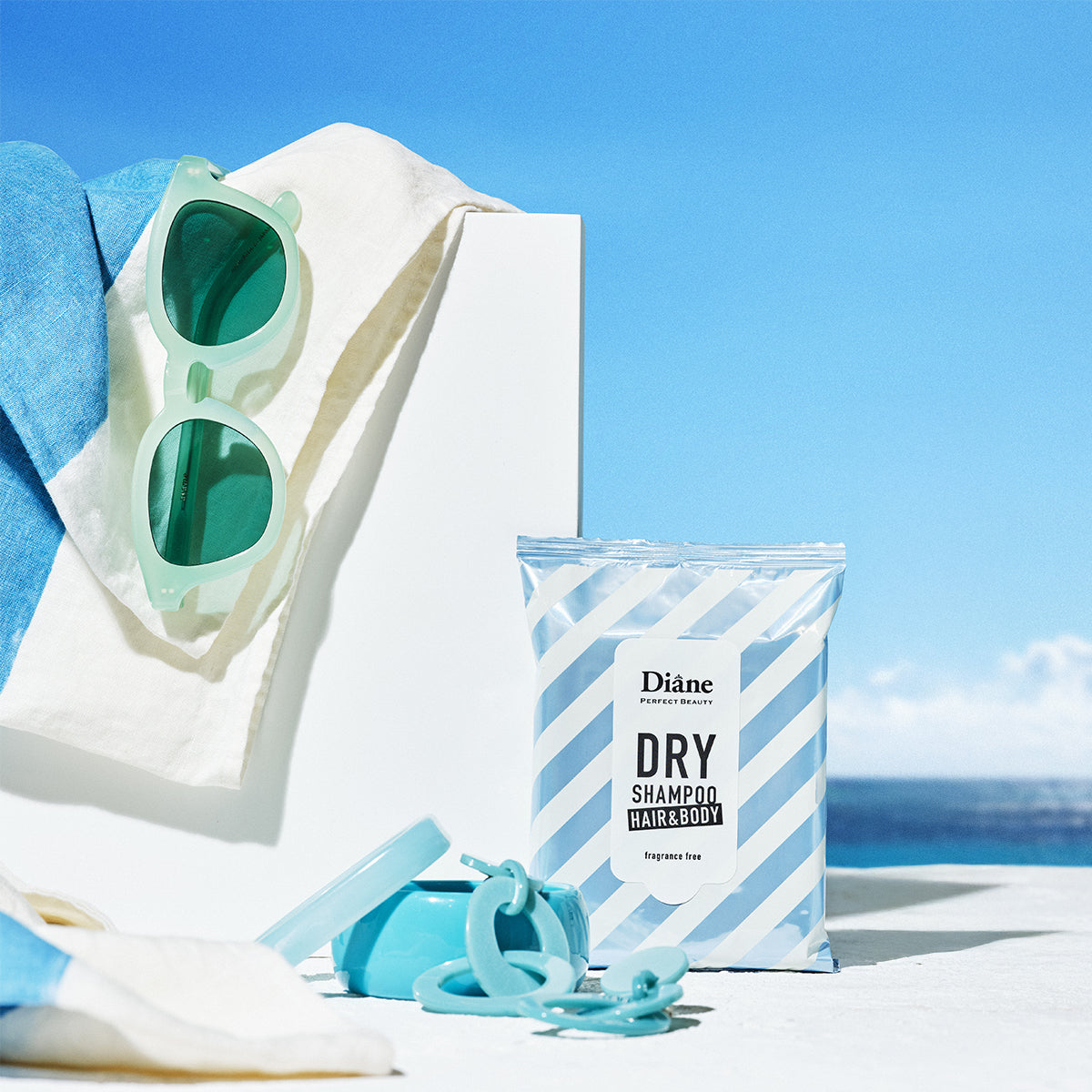 Sunglasses, towel, and Diane dry shampoo wipe on a beach with ocean view