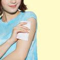 Load image into Gallery viewer, Woman applying a white mesh cloth wipe her arm against a yellow background
